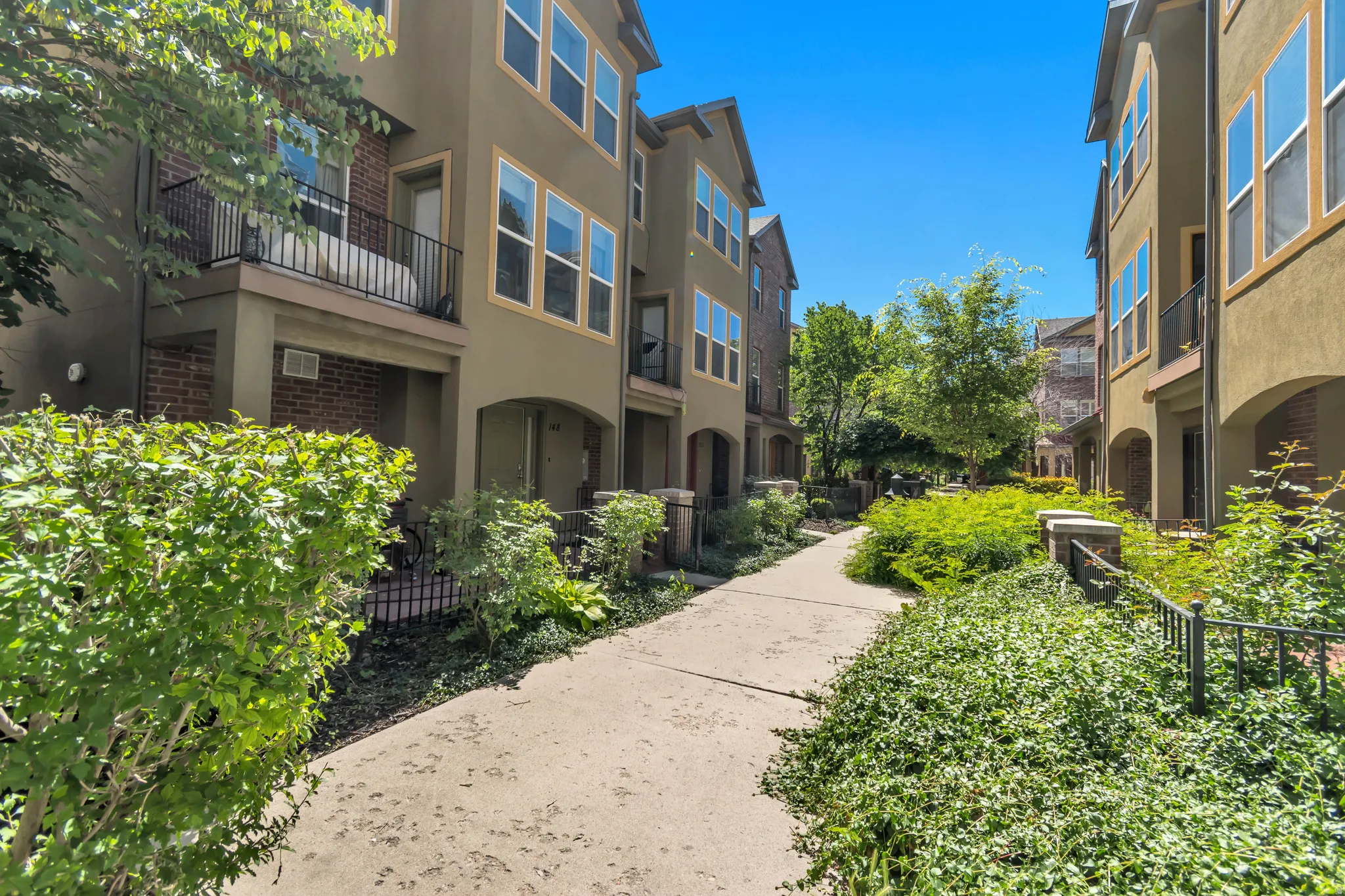 Multi-level townhome featuring a stucco exterior with brick accents, arched entryways, and upper-level balconies with black metal railings