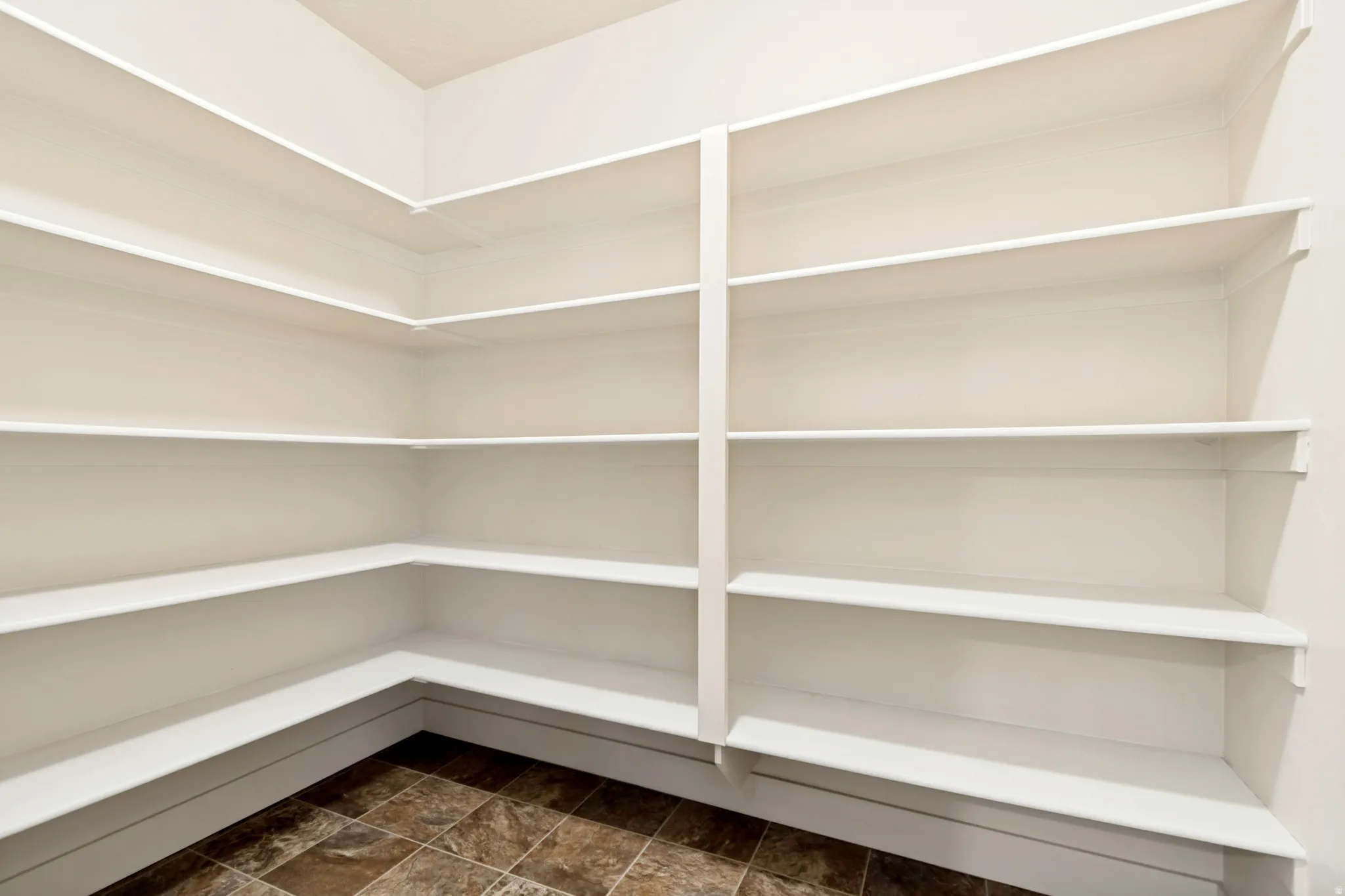 Expansive pantry featuring multi-level built-in shelving, white painted finishes, and durable tile flooring