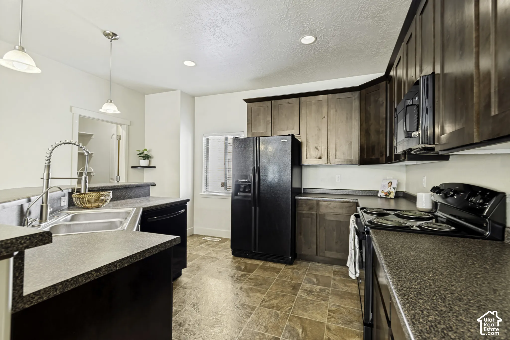 Kitchen featuring dark wood-finish cabinetry, black appliances, a double basin stainless steel sink with a high-arc faucet, and mottled gray countertops