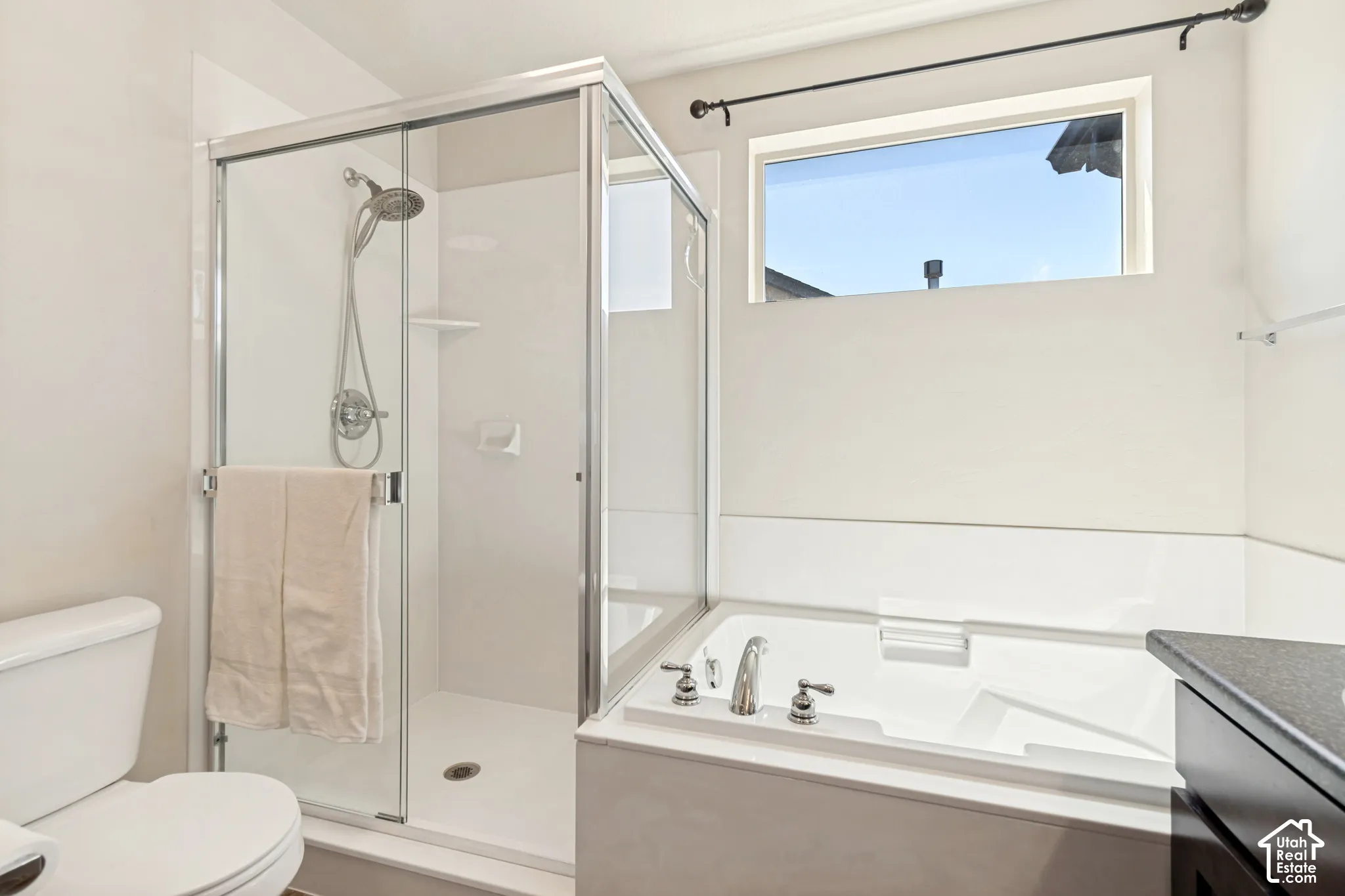 Bathroom featuring a glass-enclosed shower, a built-in soaking tub with chrome fixtures, a privacy window, and a dark-finished vanity with a stone-finish countertop