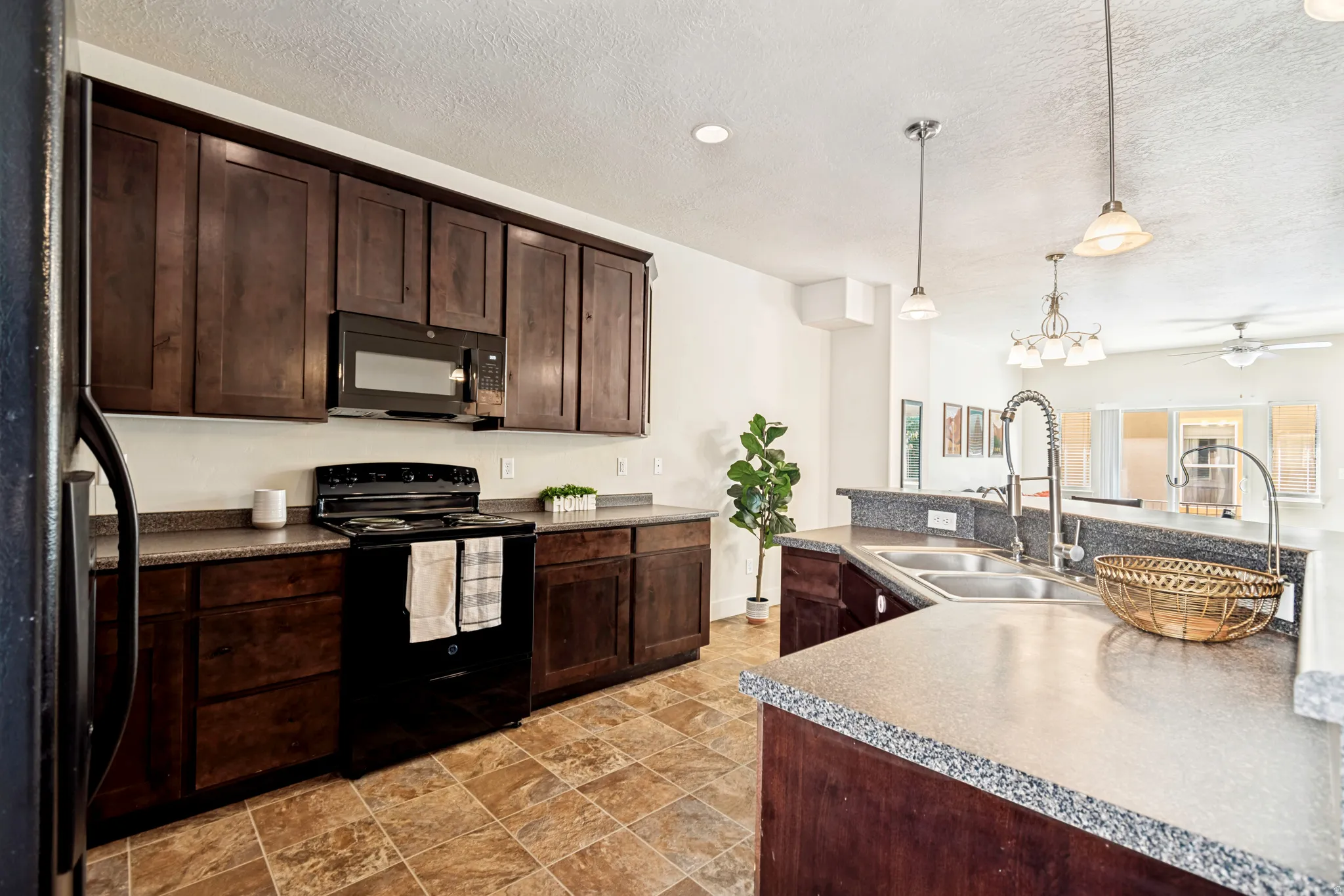 Kitchen featuring dark wood cabinetry, speckled countertops, a double basin stainless steel sink, and a combination of recessed and pendant lighting
