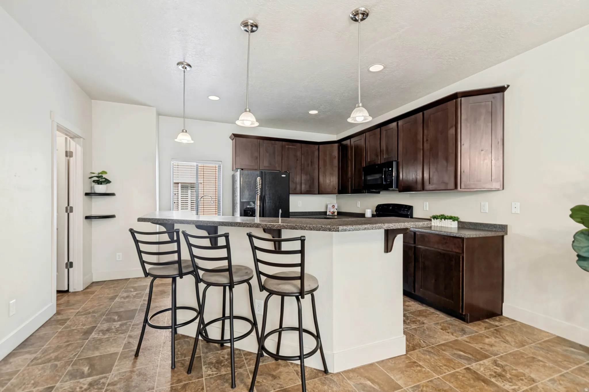 Kitchen featuring rich wood-finish cabinetry, a large peninsula with seating, speckled countertops, and an integrated black appliance package