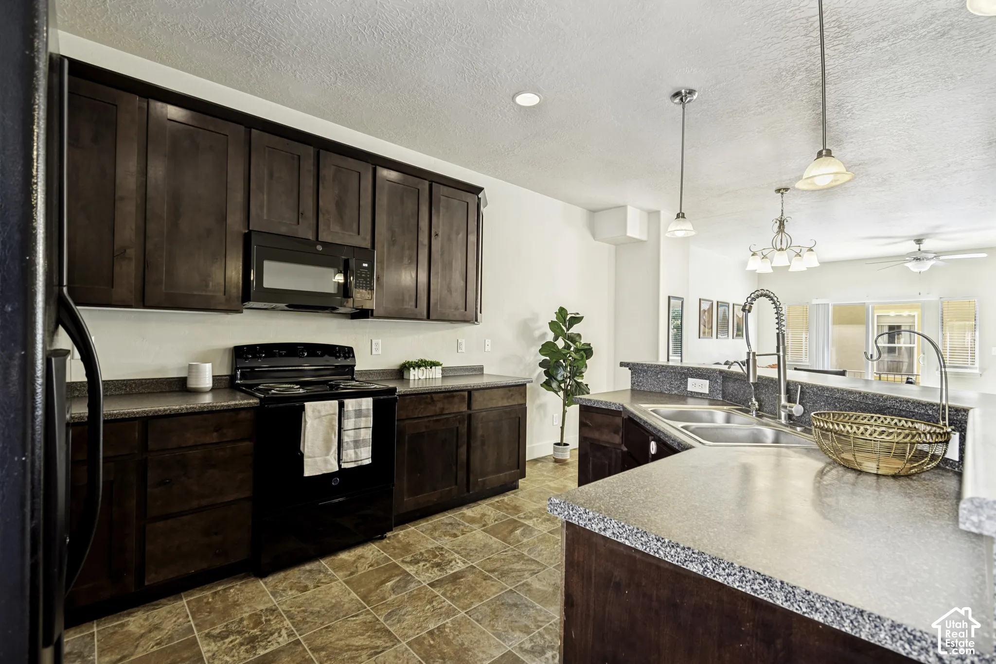 Kitchen featuring dark wood cabinetry, speckled countertops, a double basin stainless steel sink, and a combination of recessed and pendant lighting