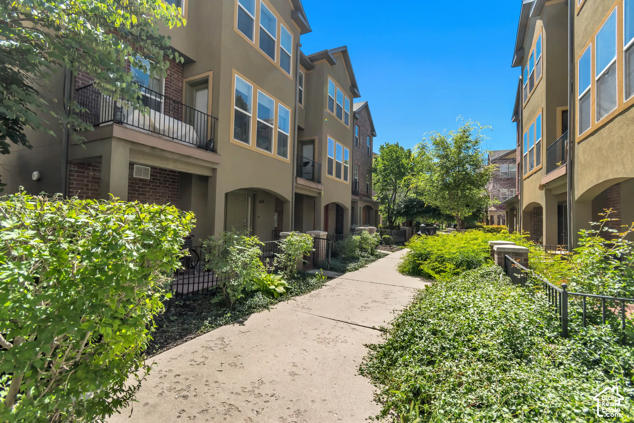 Multi-level townhome featuring a stucco exterior with brick accents, arched entryways, and upper-level balconies with black metal railings