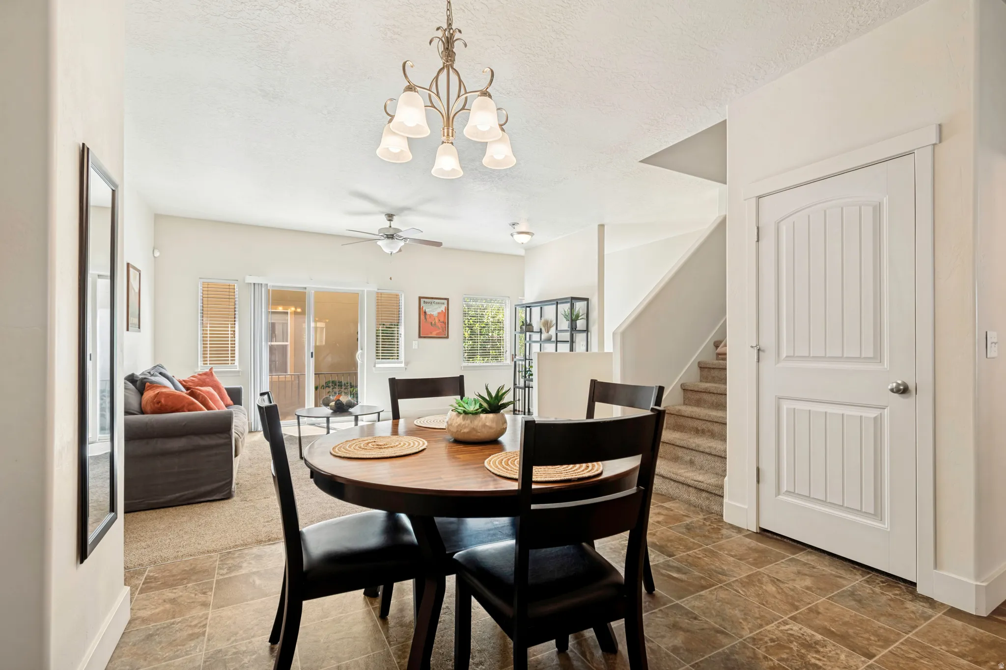 Open concept living area featuring tile flooring, a dining space with an overhead chandelier, and a living room with carpet flooring and a ceiling fan