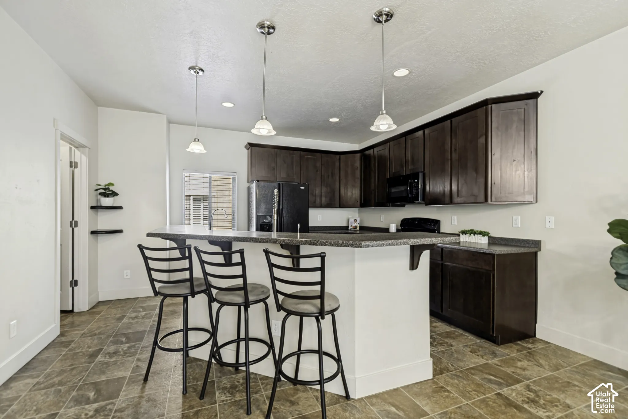 Kitchen featuring rich wood-finish cabinetry, a large peninsula with seating, speckled countertops, and an integrated black appliance package