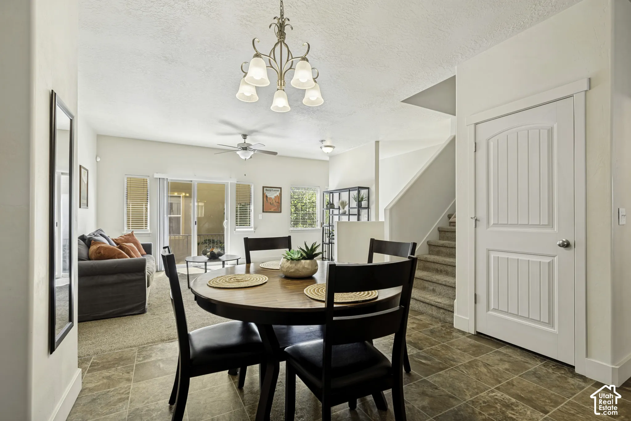 Open concept living area featuring tile flooring, a dining space with an overhead chandelier, and a living room with carpet flooring and a ceiling fan