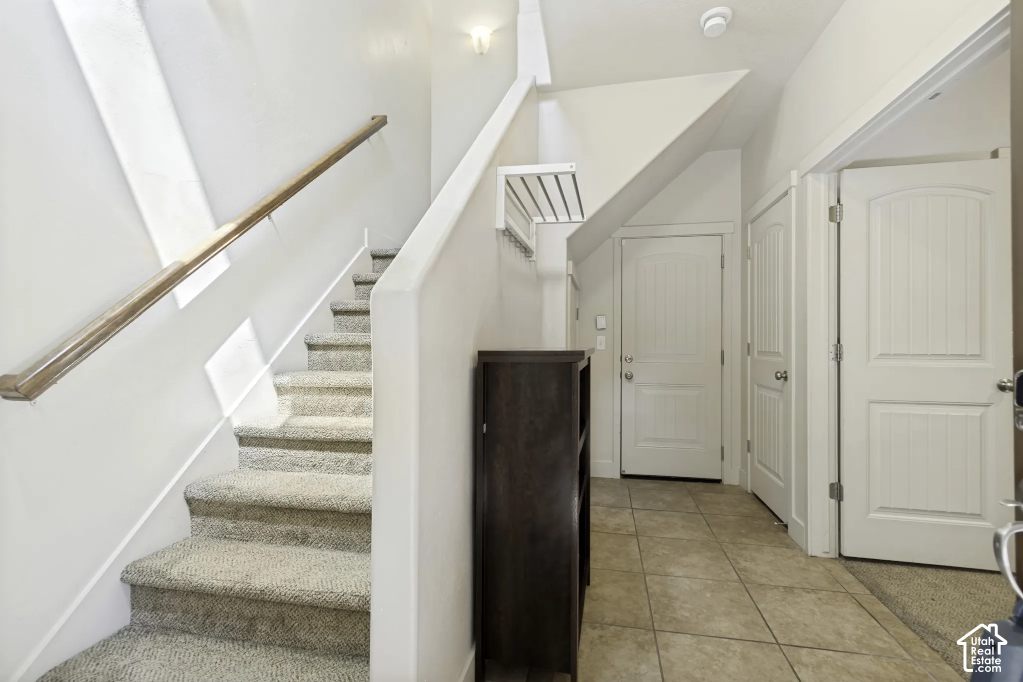 Entryway featuring tile flooring, white paneled doors, and a staircase with carpeted treads and a wood handrail