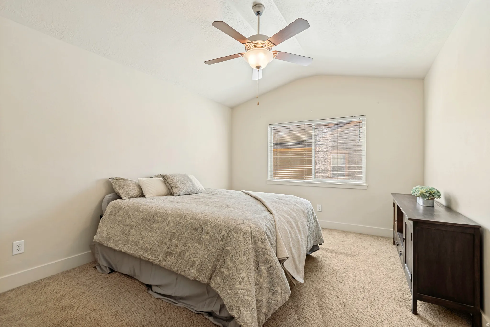 Vaulted ceiling bedroom with a ceiling fan, light-toned carpeting, and a window featuring horizontal blinds