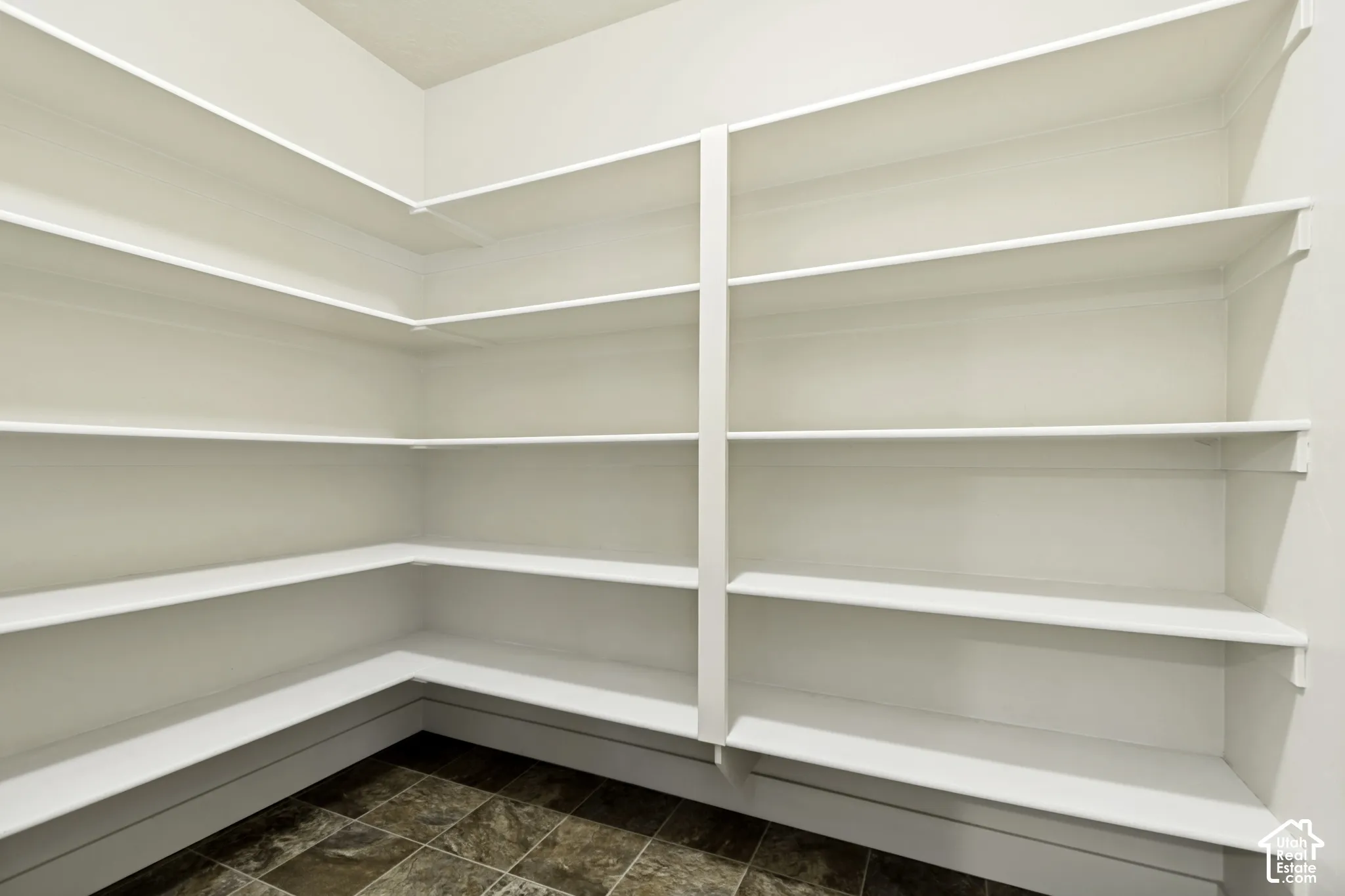 Expansive pantry featuring multi-level built-in shelving, white painted finishes, and durable tile flooring