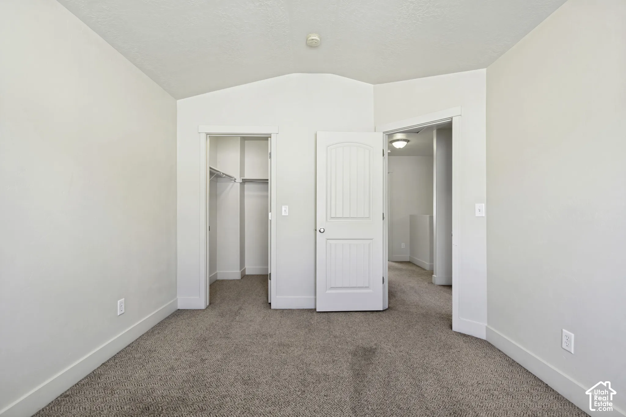 Carpeted room featuring a vaulted ceiling, a closet with wire shelving, and a white paneled door