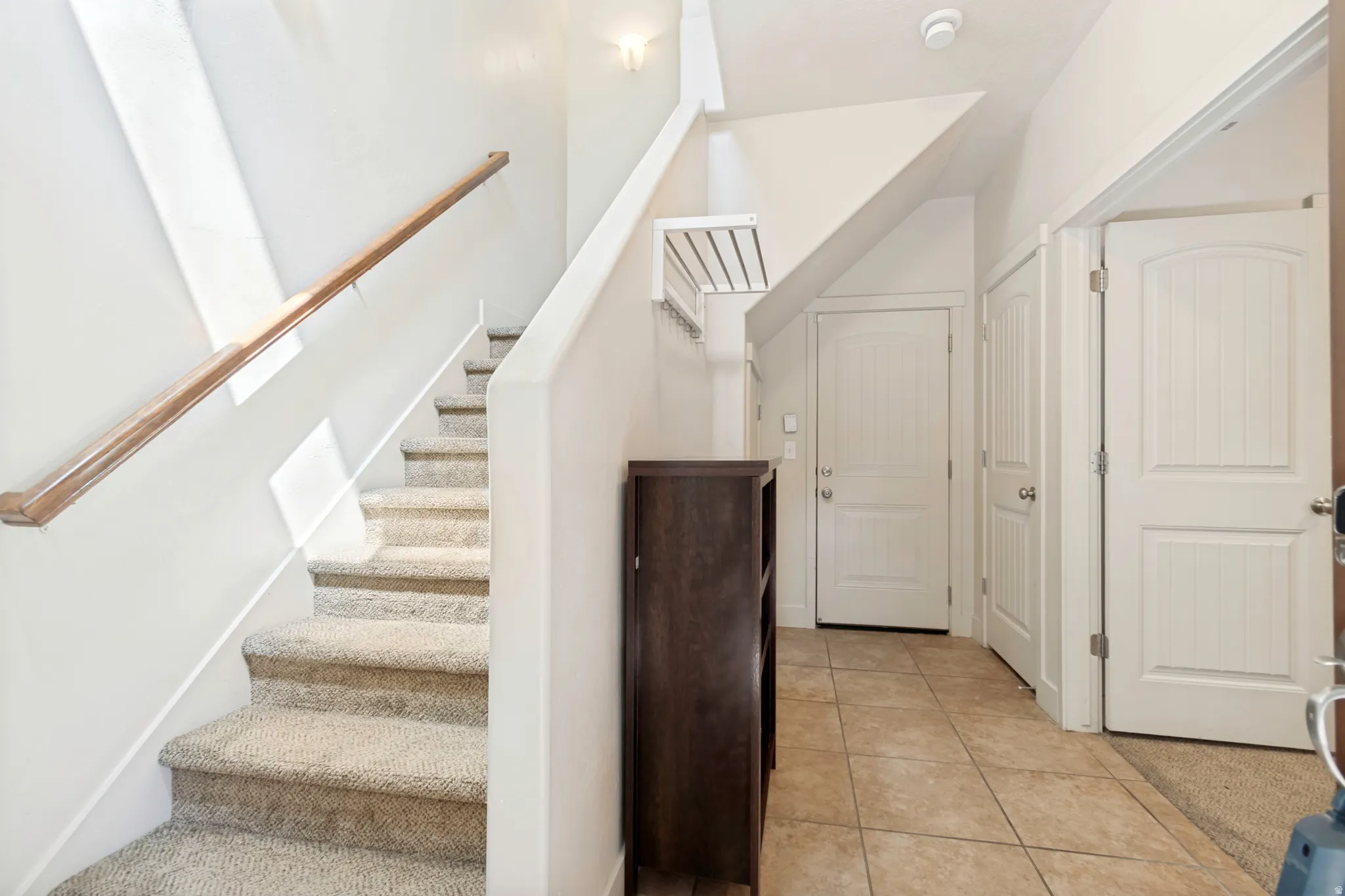 Entryway featuring tile flooring, white paneled doors, and a staircase with carpeted treads and a wood handrail