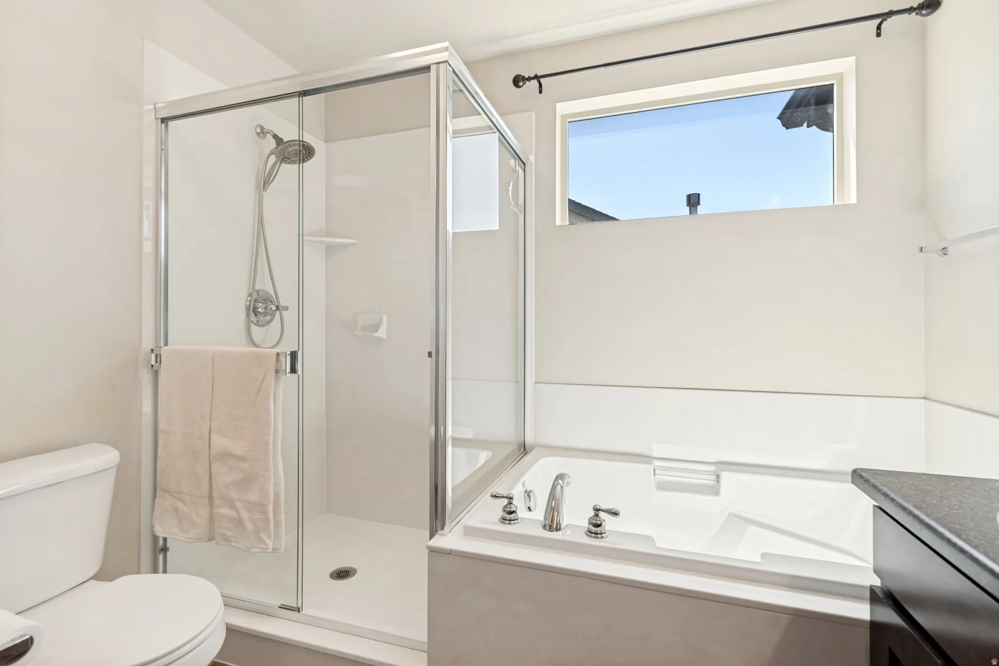 Bathroom featuring a glass-enclosed shower, a built-in soaking tub with chrome fixtures, a privacy window, and a dark-finished vanity with a stone-finish countertop