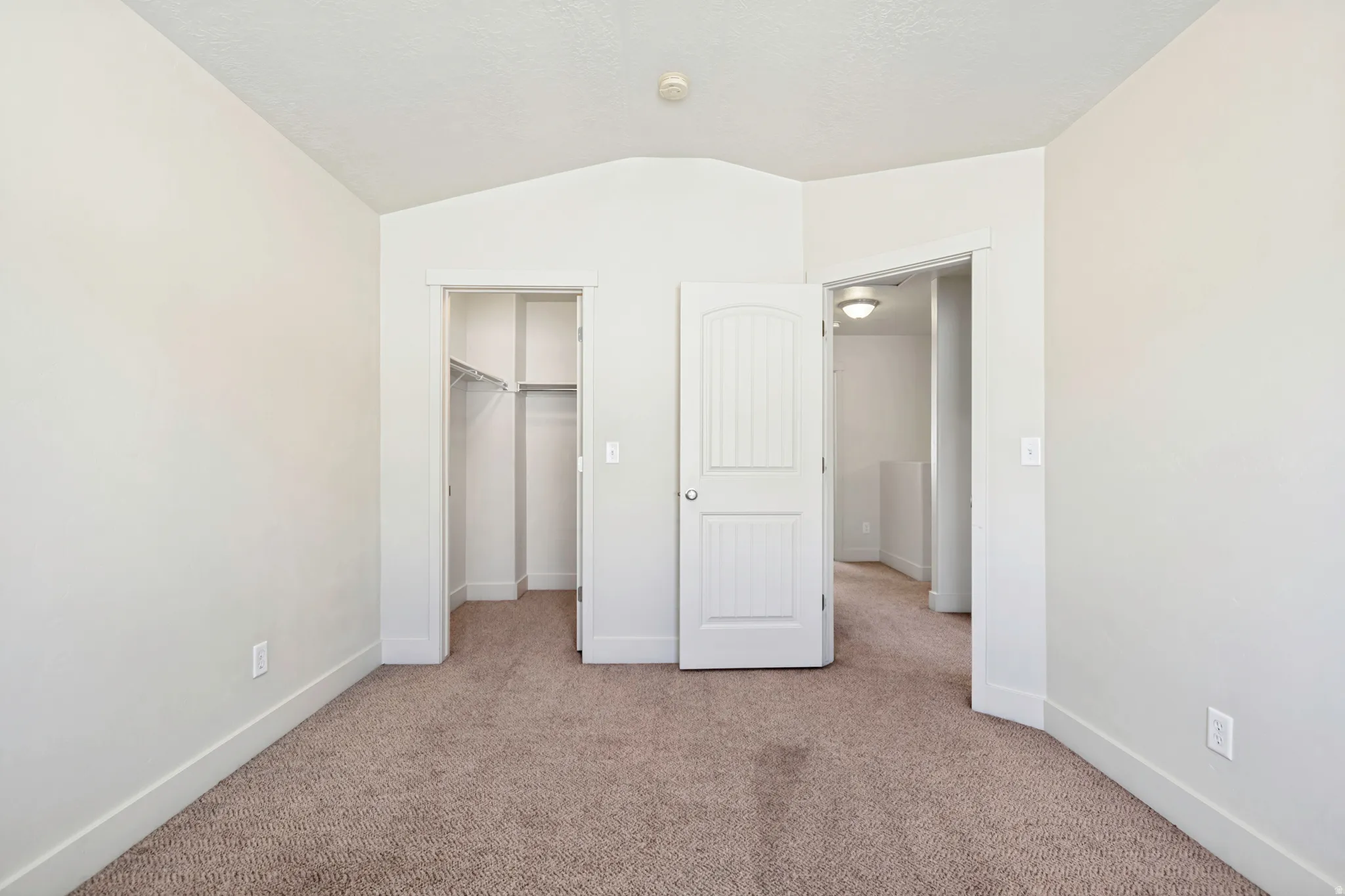 Carpeted room featuring a vaulted ceiling, a closet with wire shelving, and a white paneled door