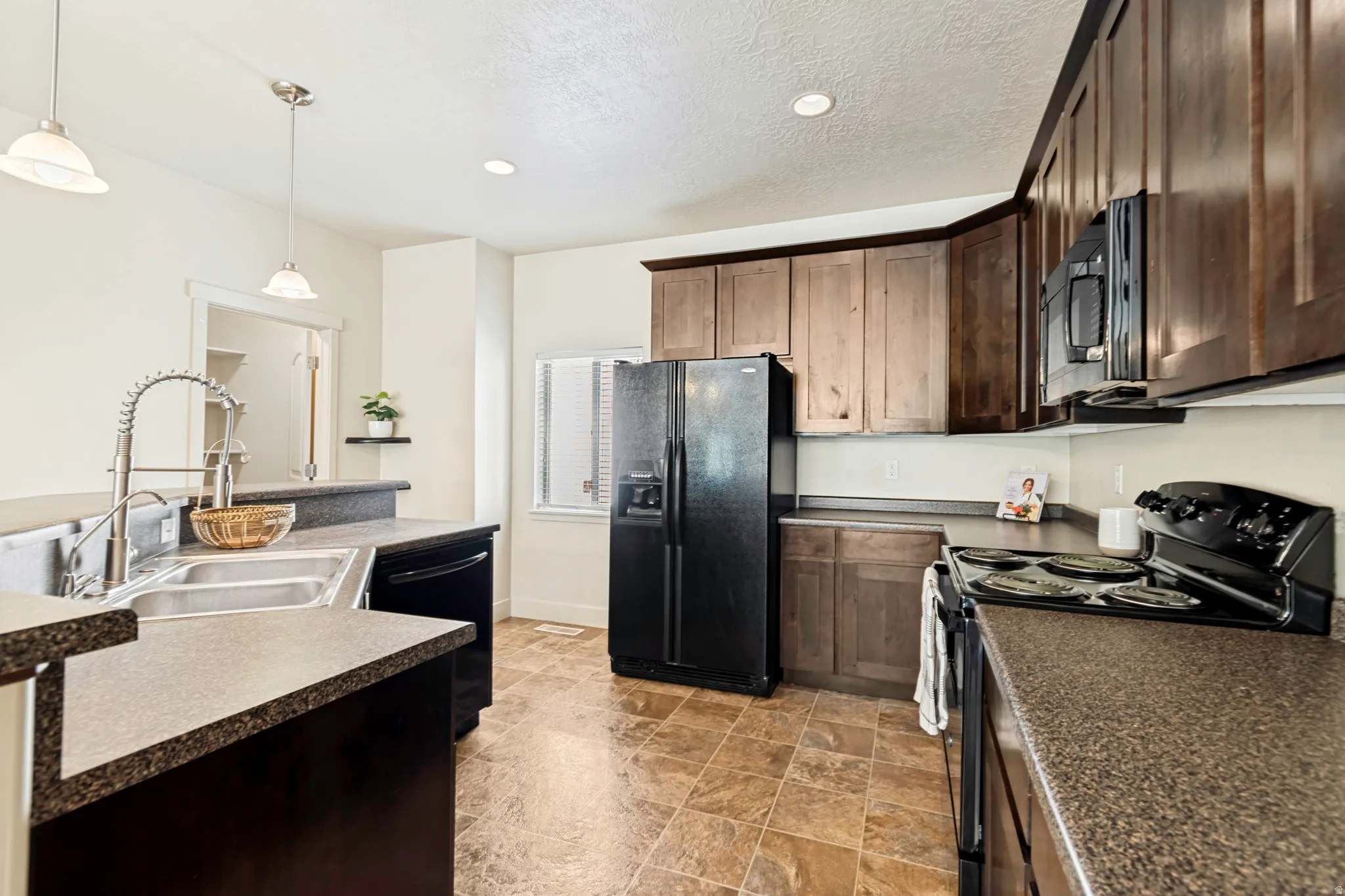 Kitchen featuring dark wood-finish cabinetry, black appliances, a double basin stainless steel sink with a high-arc faucet, and mottled gray countertops