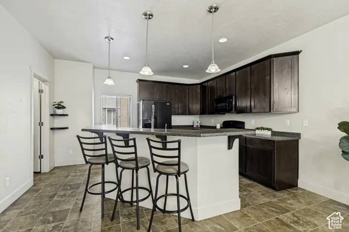 Kitchen featuring rich wood-finish cabinetry, a large peninsula with seating, speckled countertops, and an integrated black appliance package