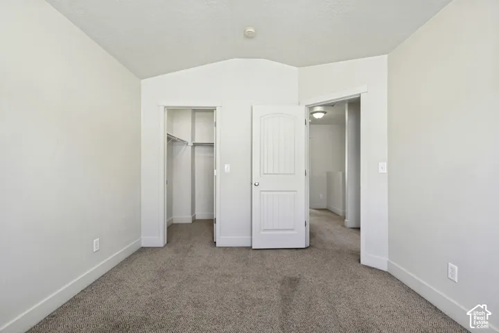 Carpeted room featuring a vaulted ceiling, a closet with wire shelving, and a white paneled door