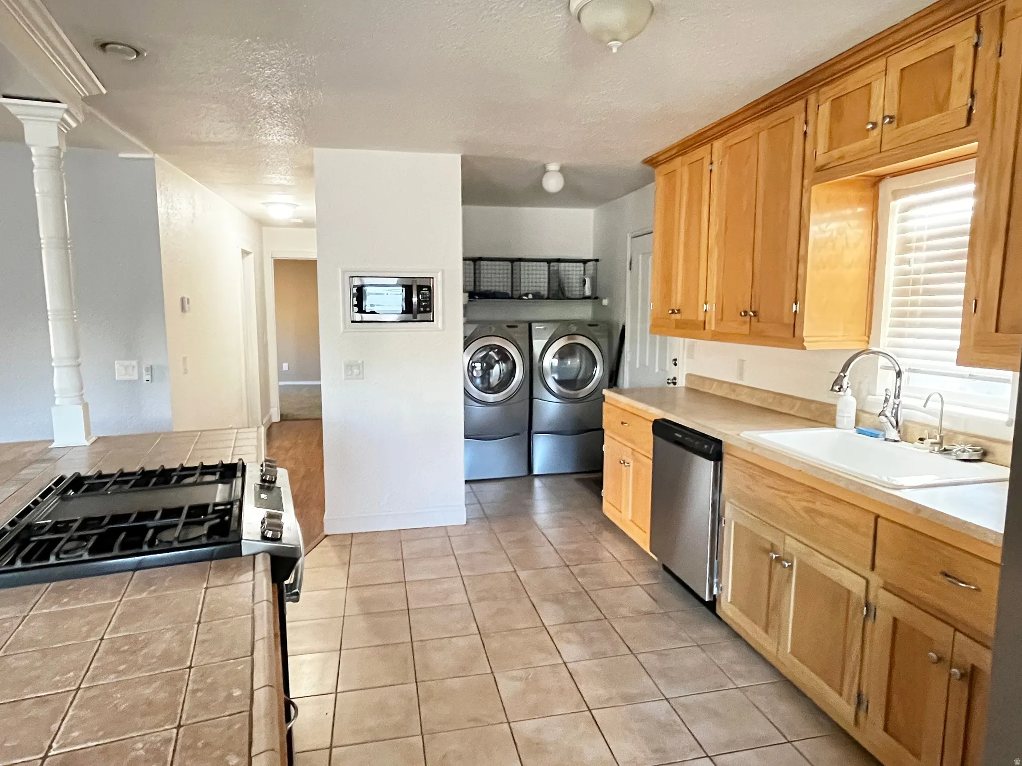 Kitchen with tile flooring and wood cabinetry, featuring a gas range, built-in microwave, stainless steel dishwasher, and a double basin sink with a gooseneck faucet