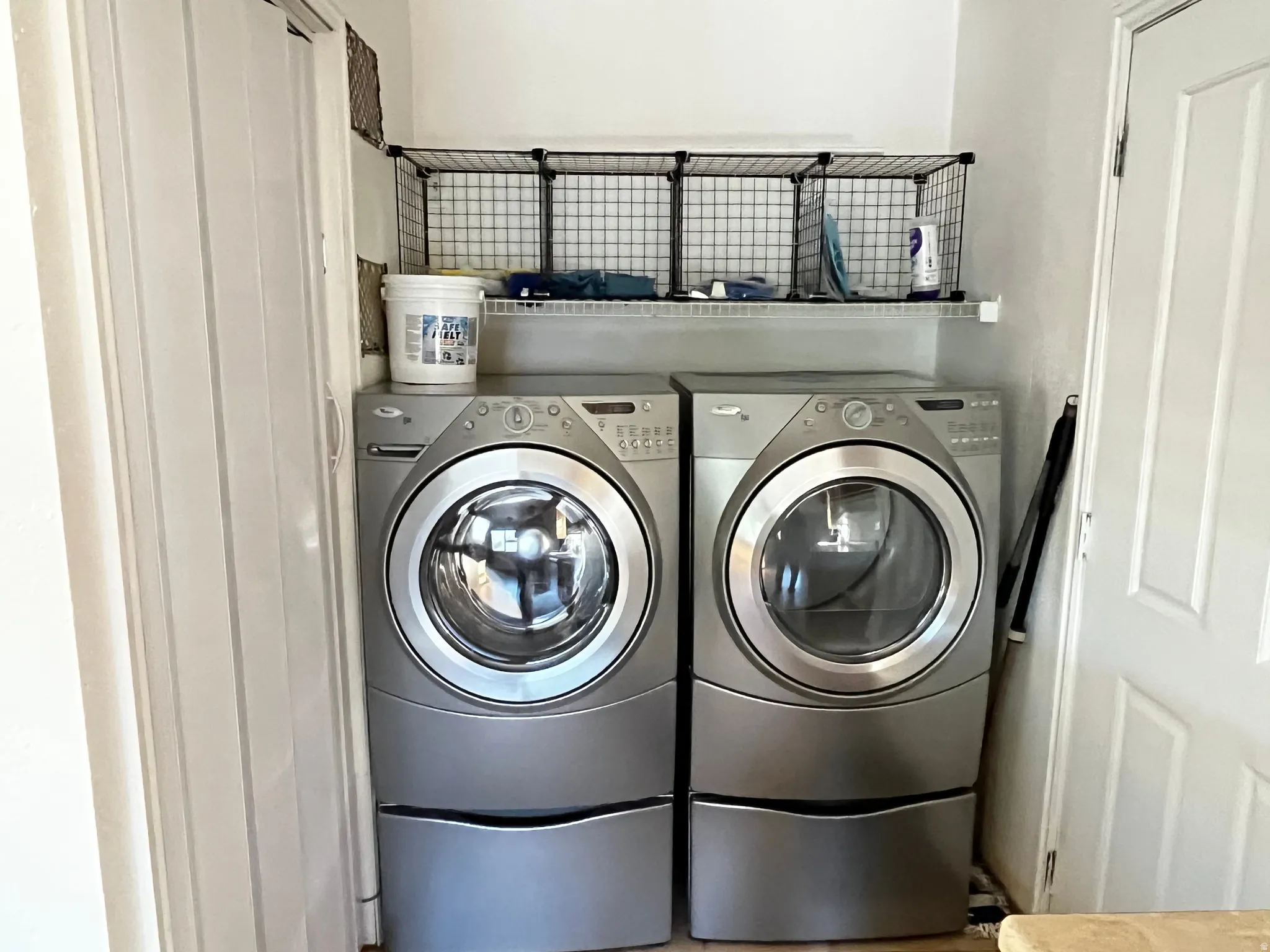 Dedicated laundry area featuring front-loading appliances, an overhead storage shelf, and open wire shelving