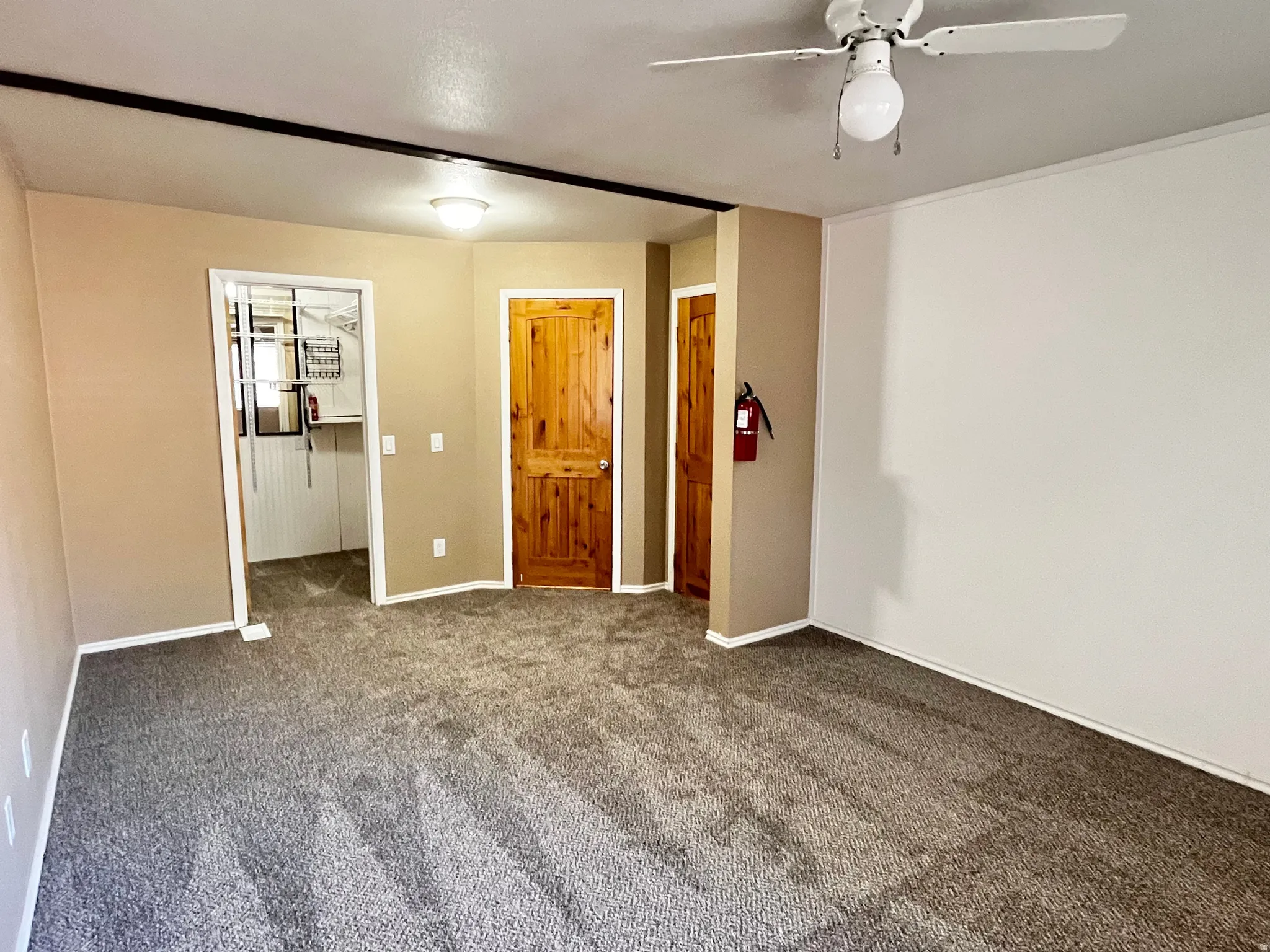 Spacious room featuring neutral-toned walls, contrasting wood-finish interior doors, and a ceiling fan with integrated lighting