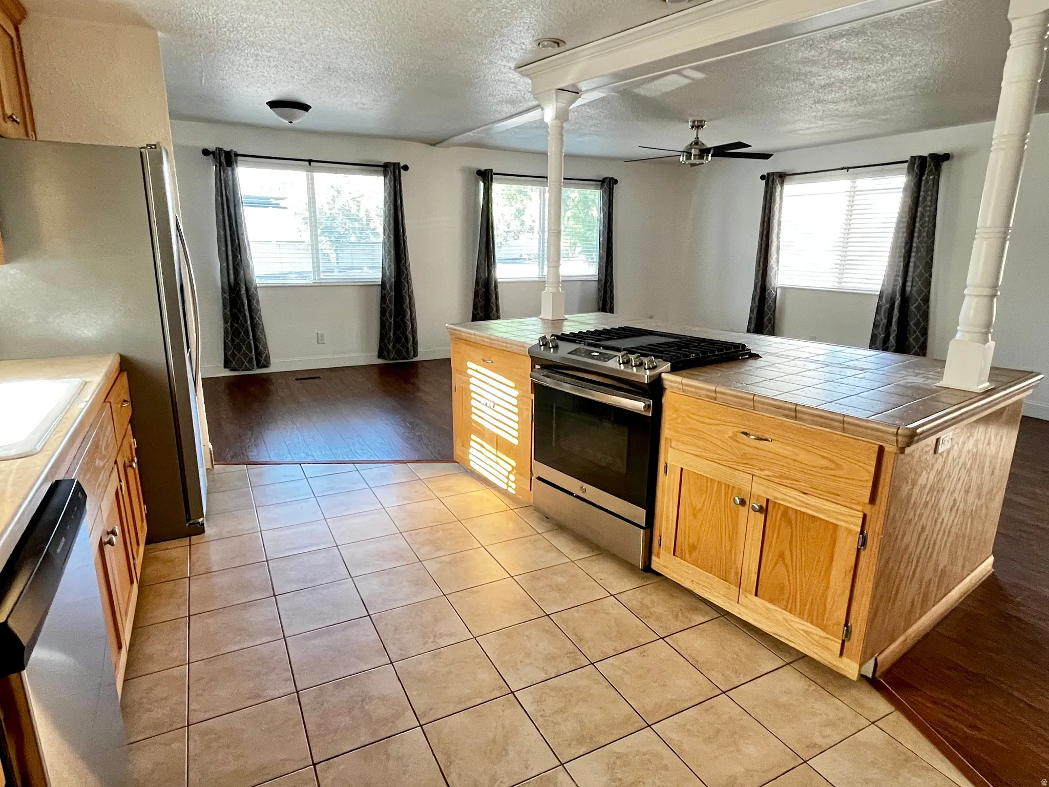 Open-concept kitchen featuring a tile-top island with a built-in stainless steel oven/range, light wood cabinetry, and tile flooring