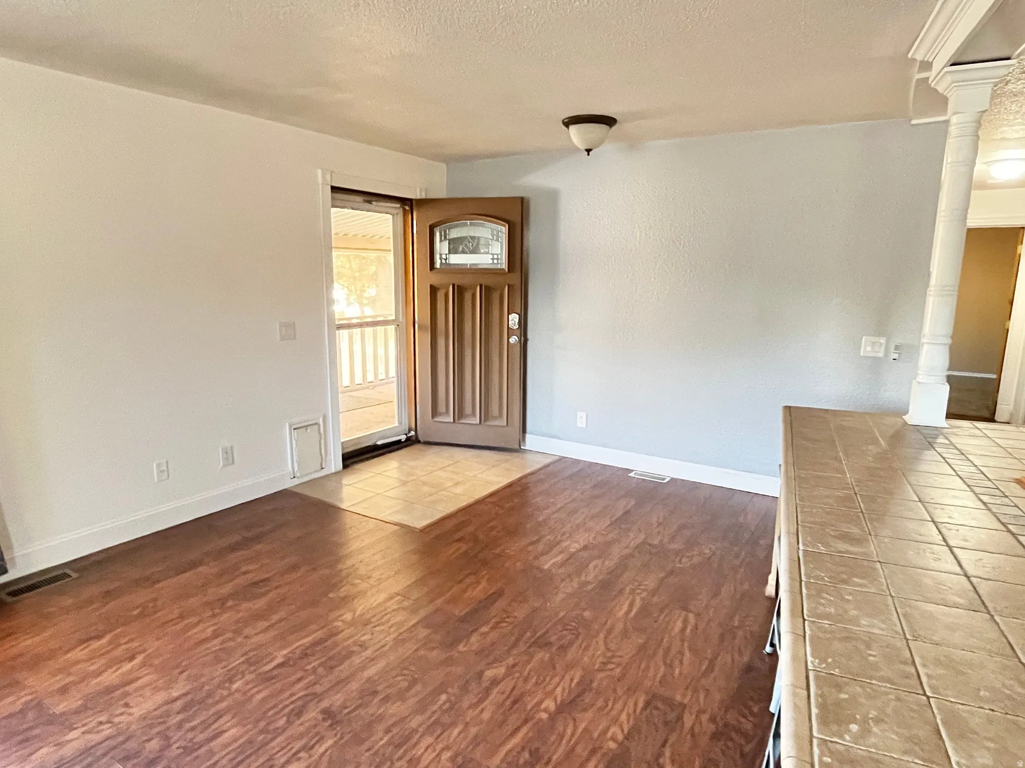 Entryway featuring a decorative wood-panel door with an arched glass insert, tiled landing, and wood-finish flooring