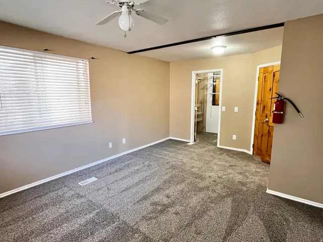 Spacious interior featuring neutral-toned walls, patterned carpeting, and a ceiling fan with integrated lighting