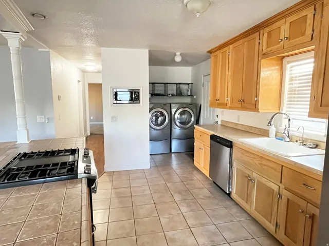 Kitchen with tile flooring and wood cabinetry, featuring a gas range, built-in microwave, stainless steel dishwasher, and a double basin sink with a gooseneck faucet