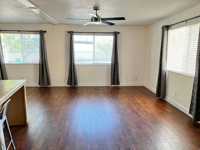 Spacious interior featuring rich wood-finish flooring, multiple windows with blinds, a ceiling fan, and white baseboards