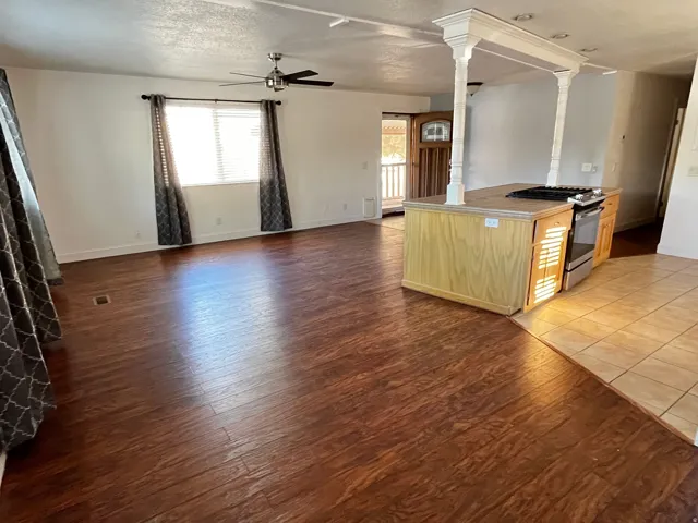 Spacious living area featuring wood-finish flooring, a ceiling fan, and window blinds