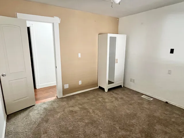 Room featuring neutral-toned walls and plush carpeting, with a white paneled door opening to an adjacent space with wood-finish flooring