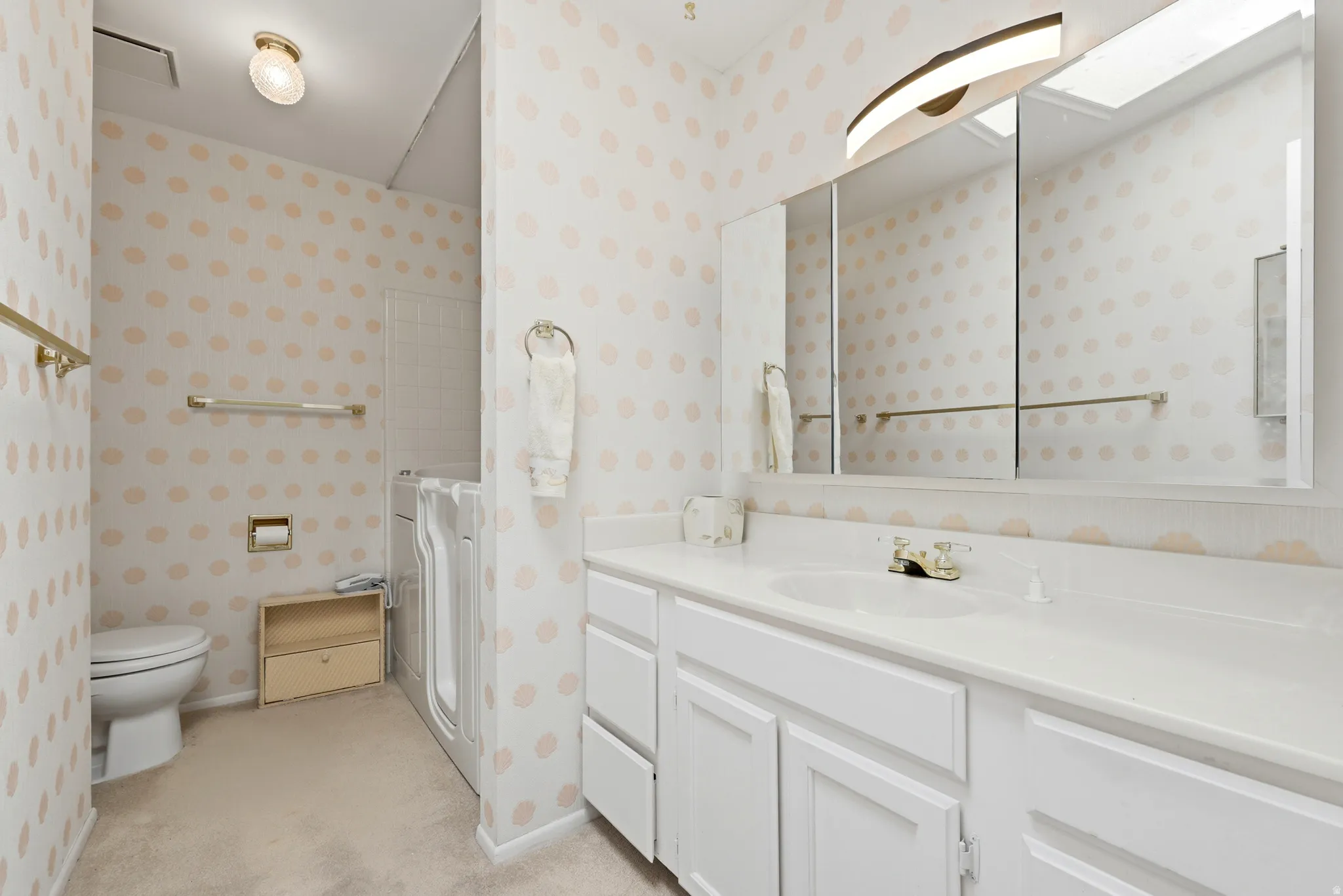 Bathroom featuring a dual-sink vanity with white cabinetry, a large mirrored medicine cabinet with integrated lighting, a toilet, and a built-in shower with a white access panel