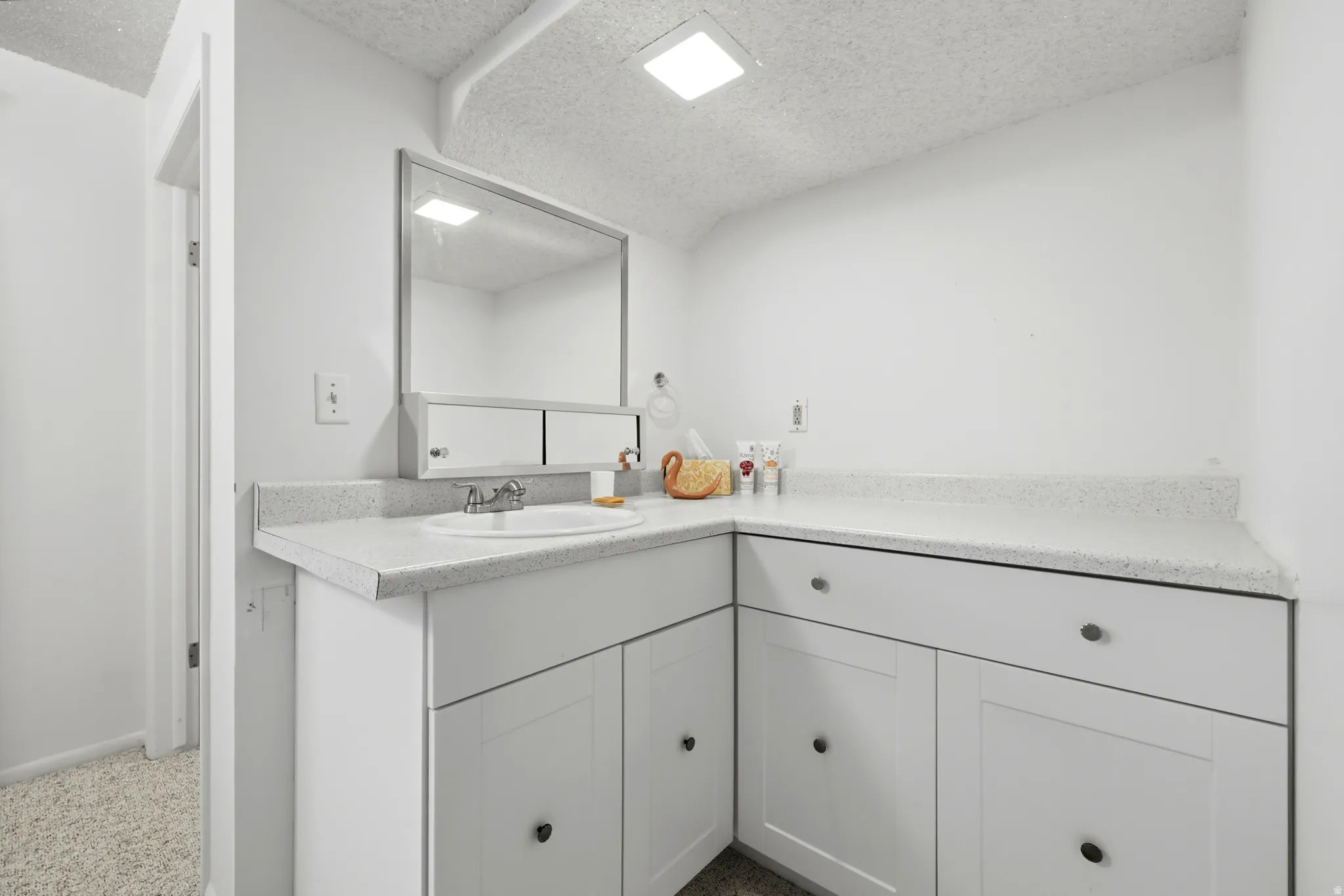 Bathroom vanity featuring a white countertop with integrated sink, chrome faucet, and expansive wall-mounted mirror
