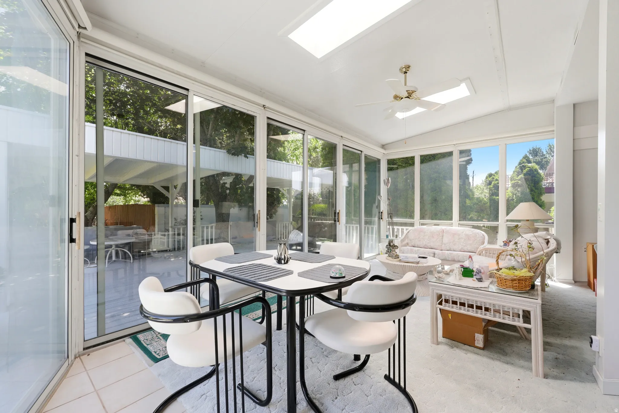 Sunroom featuring a vaulted ceiling with skylights and a ceiling fan, extensive sliding glass doors, white tiled flooring, and an exterior covered patio area