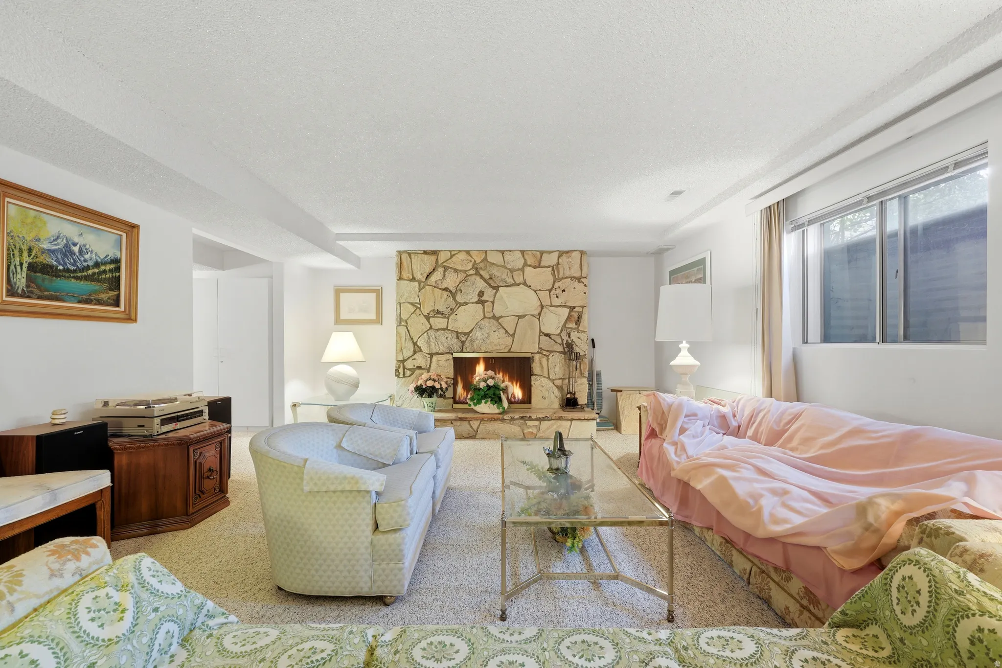 Living area featuring a stone-clad fireplace, light-toned carpet flooring, and a large window providing natural light