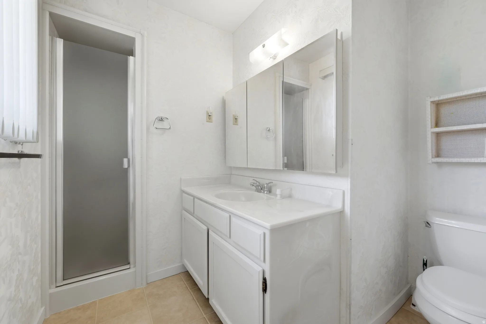Bathroom featuring a shower with frosted glass enclosure, single vanity with white cabinetry and countertop, recessed medicine cabinet, and a wall-mounted shelving unit