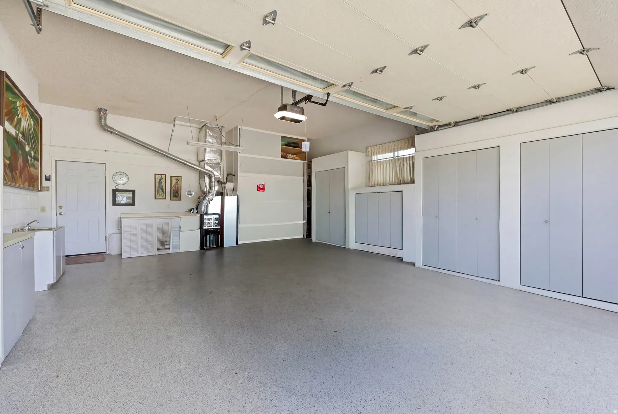 Spacious garage featuring expansive storage cabinetry, a utility sink with white cabinetry, a dedicated side entry door, and an overhead garage door