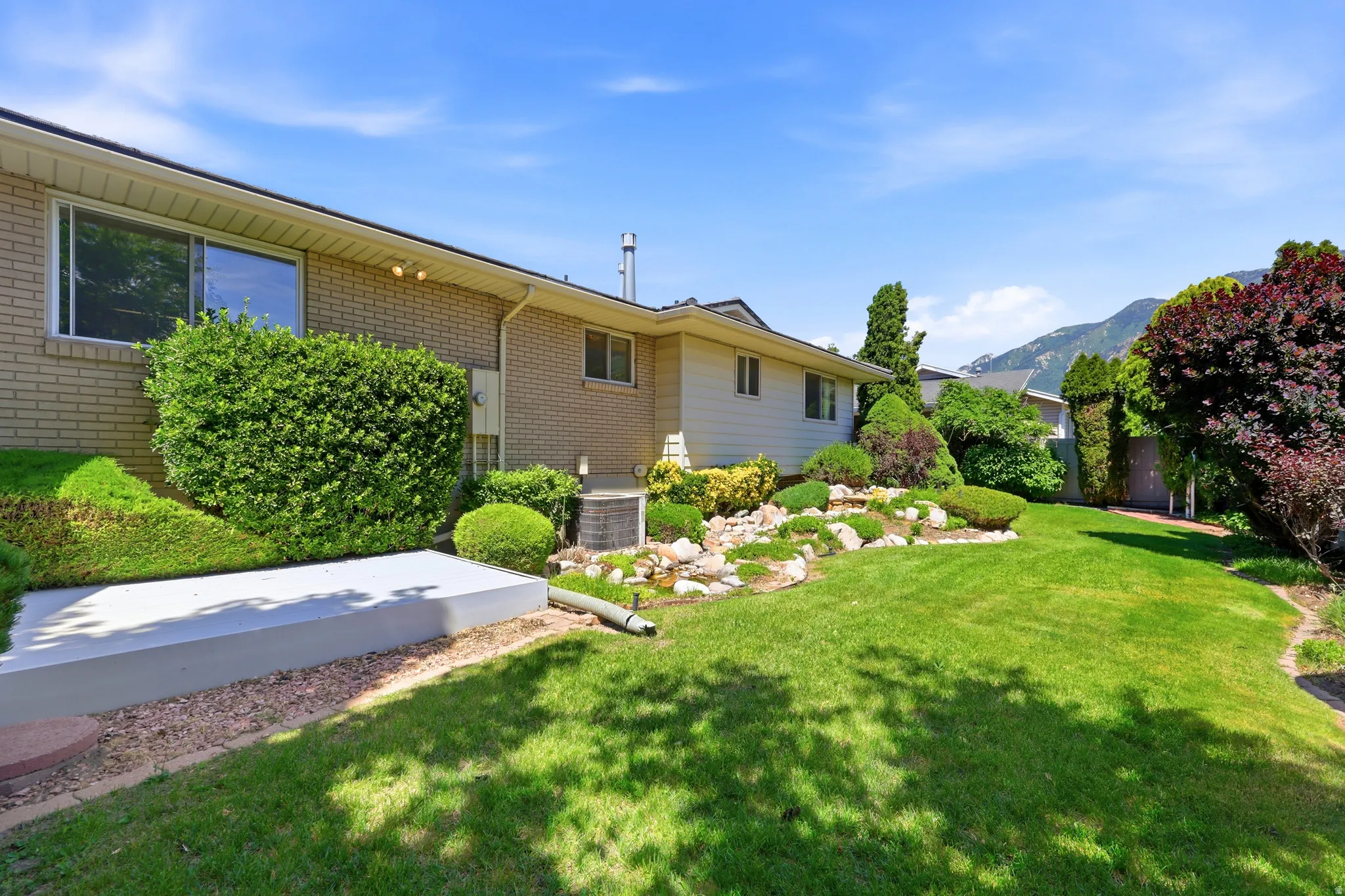 Expansive green lawn with established landscaping, featuring a rock garden and mature trees