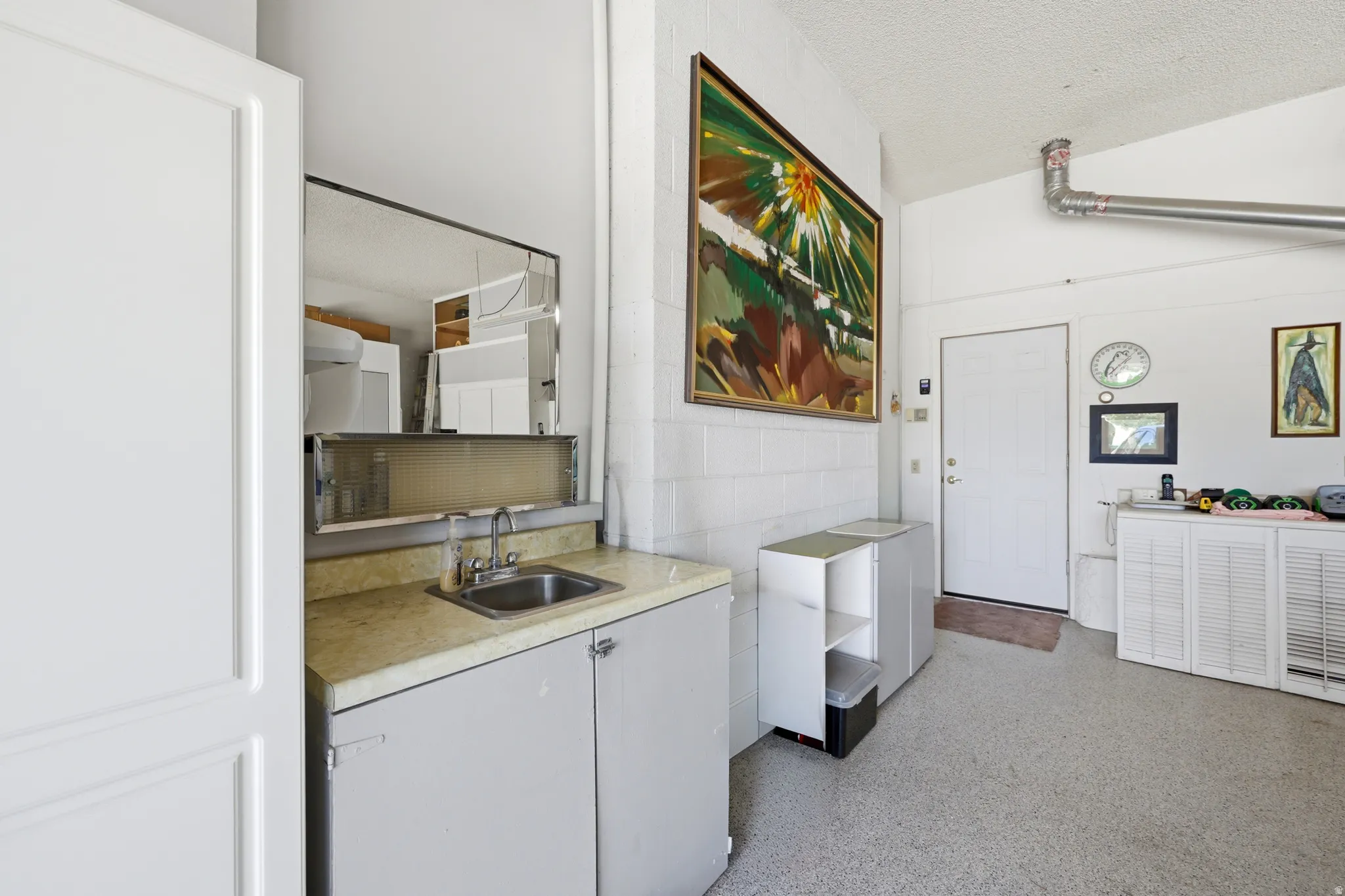 Utility area featuring a stainless steel sink, light-toned countertop, and white cabinetry