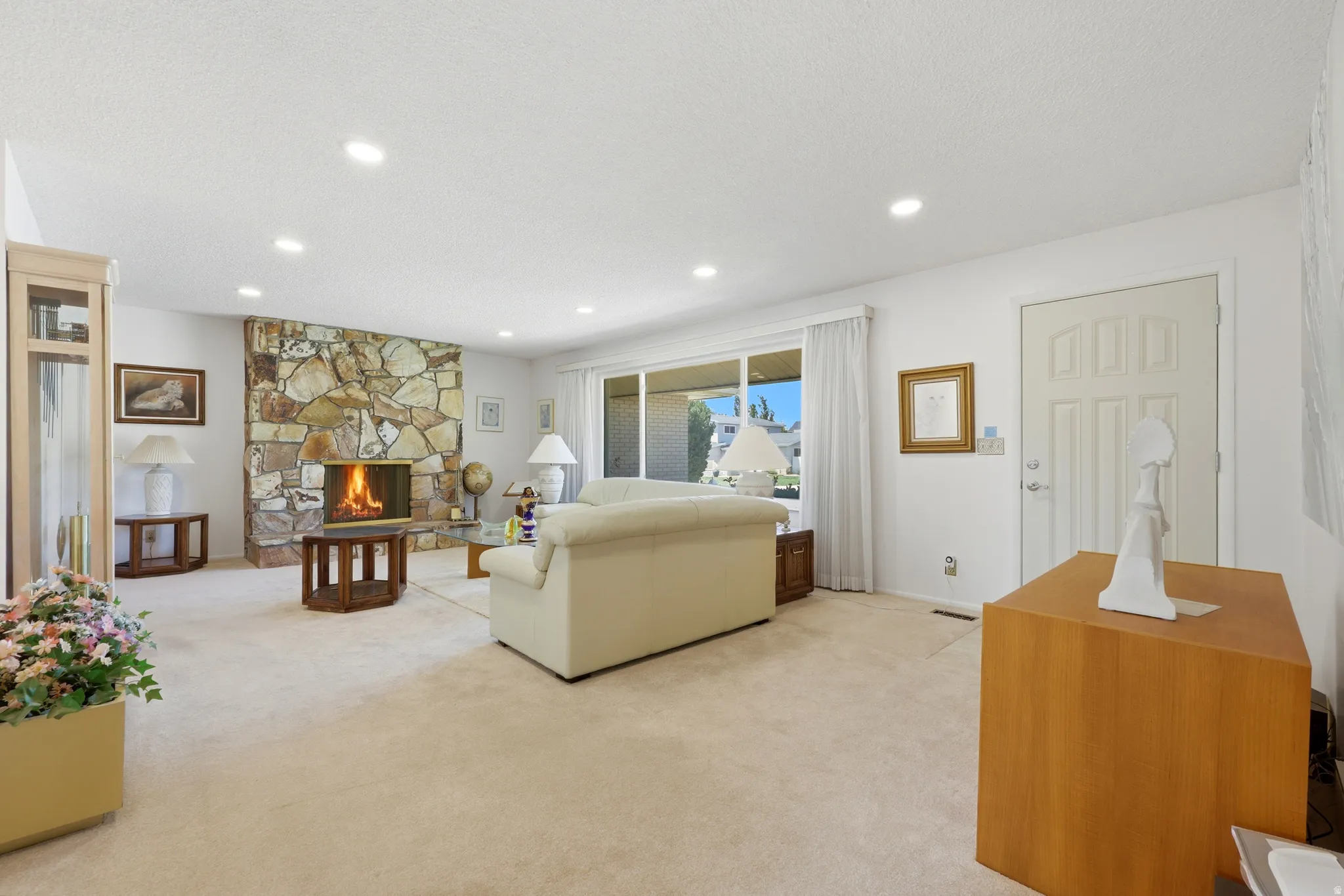 Living area featuring a stone-clad fireplace, recessed lighting, expansive windows, and a paneled entry door