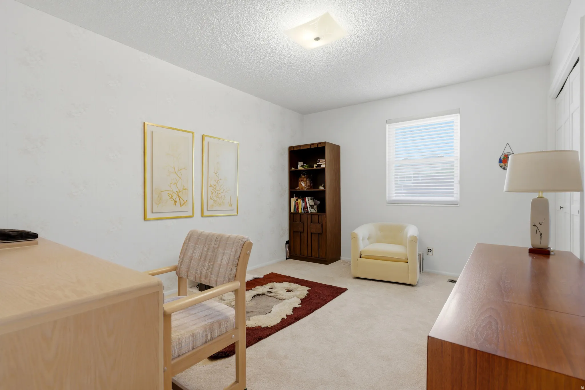 Carpeted interior room featuring a single window with horizontal blinds, built-in overhead lighting, and white walls