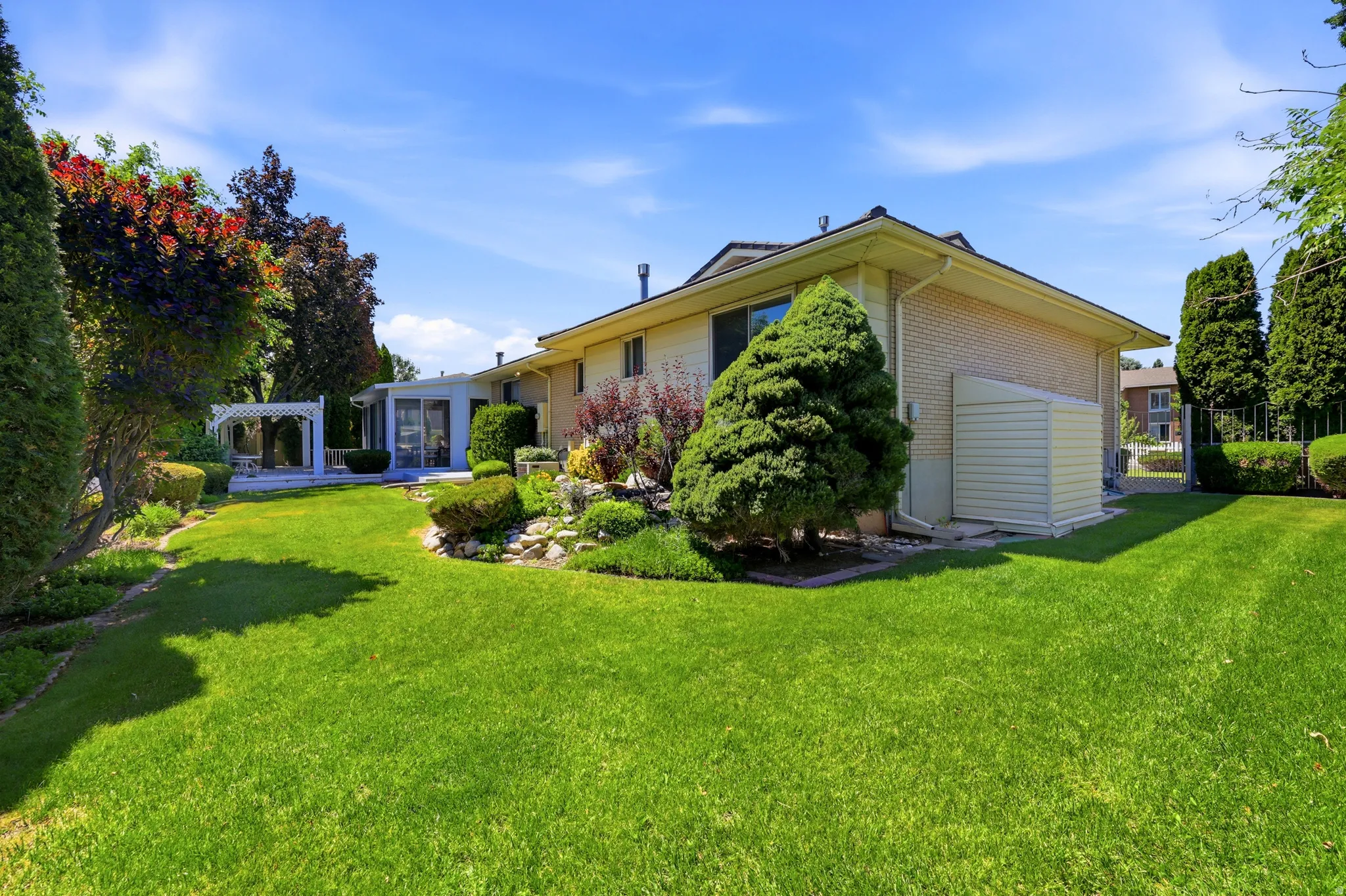 Expansive rear yard featuring a vibrant lawn, mature perimeter landscaping, and a white pergola