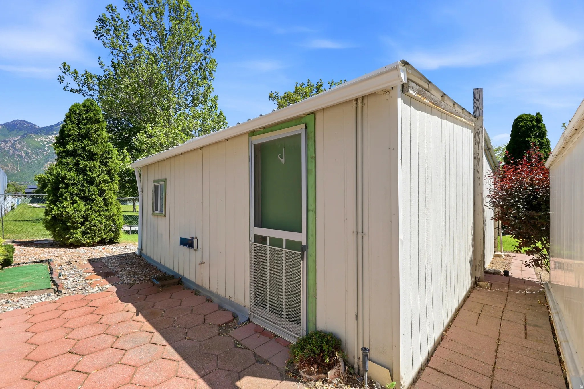 Utility shed with vertical siding and a screen door, complemented by a paver patio