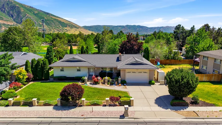 Ranch-style residence featuring a prominent front lawn, mature landscaping, and an attached two-car garage