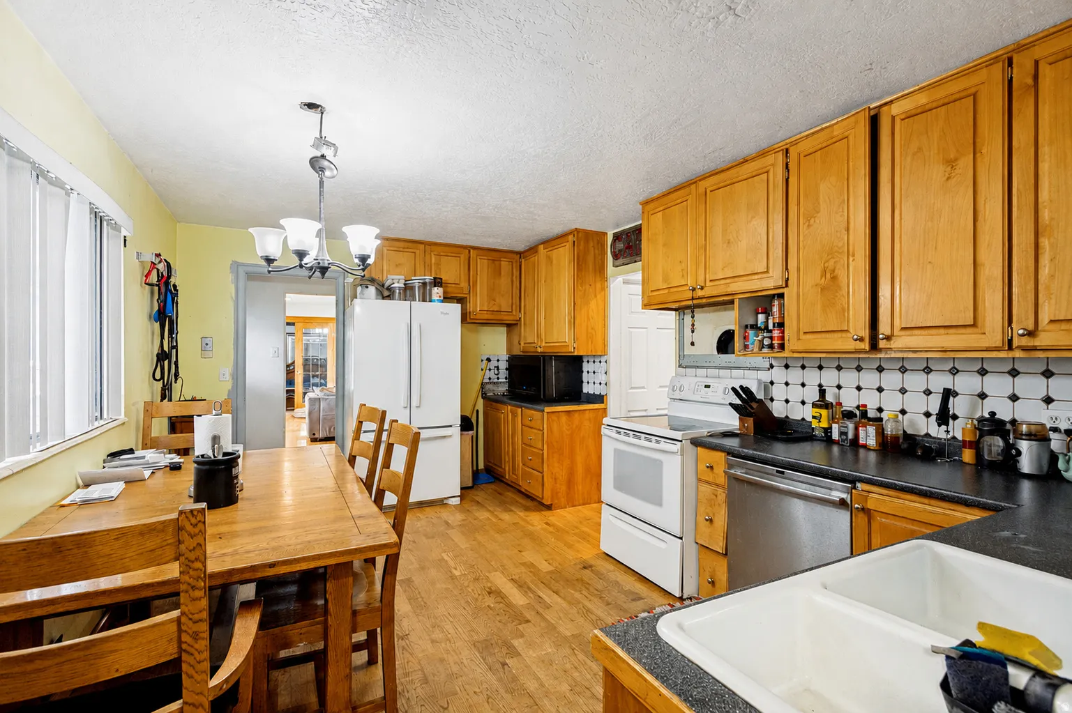 Kitchen featuring wood-finish flooring, natural wood cabinetry, a double basin sink, and white appliances