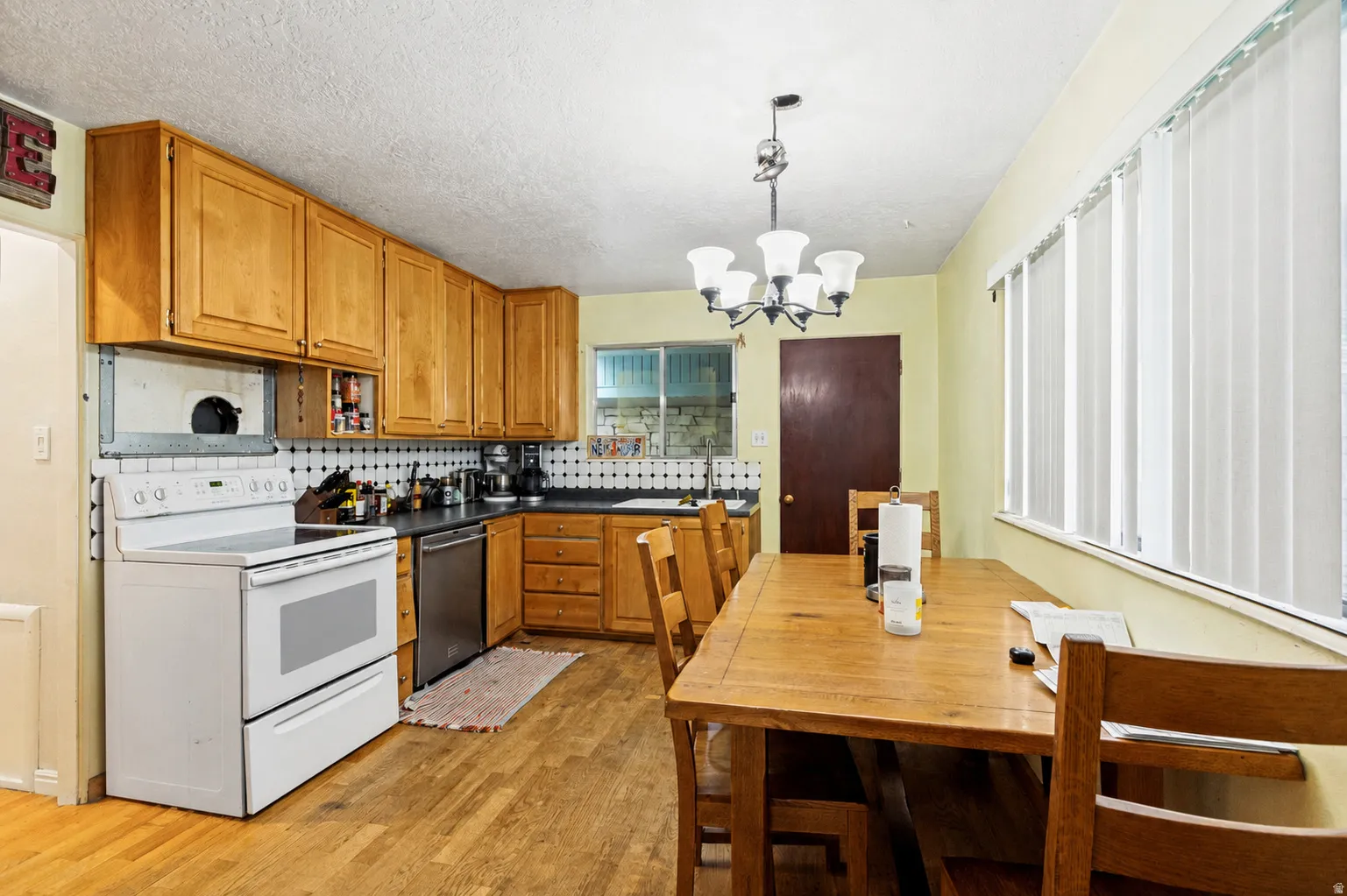 Kitchen featuring wood-finish flooring, wood cabinetry, a white electric range, a stainless steel dishwasher, and a black countertop
