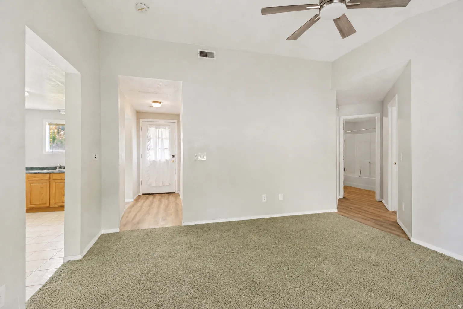 Vaulted family room looking back to entry, with kitchen on one side and hall to two bedrooms and bath on the other.