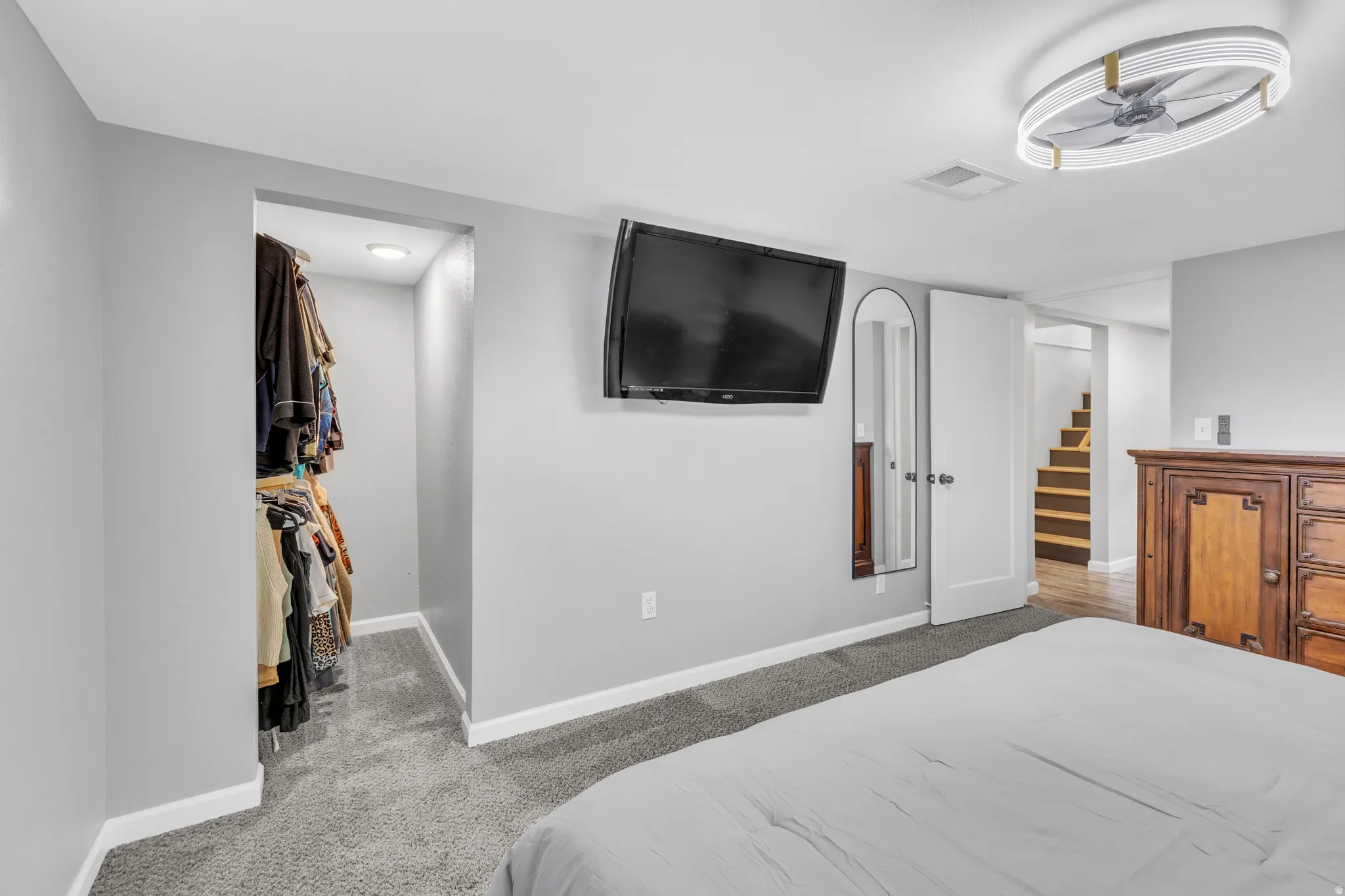 Carpeted bedroom featuring a flush-mount ceiling fan with integrated lighting, a wall-mounted television, and a built-in closet with recessed lighting