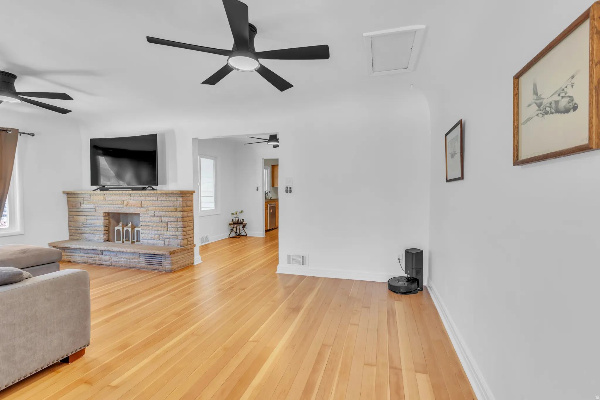 Bright living space featuring natural wood-finish flooring, a stone-clad fireplace, and two ceiling fans with integrated lighting