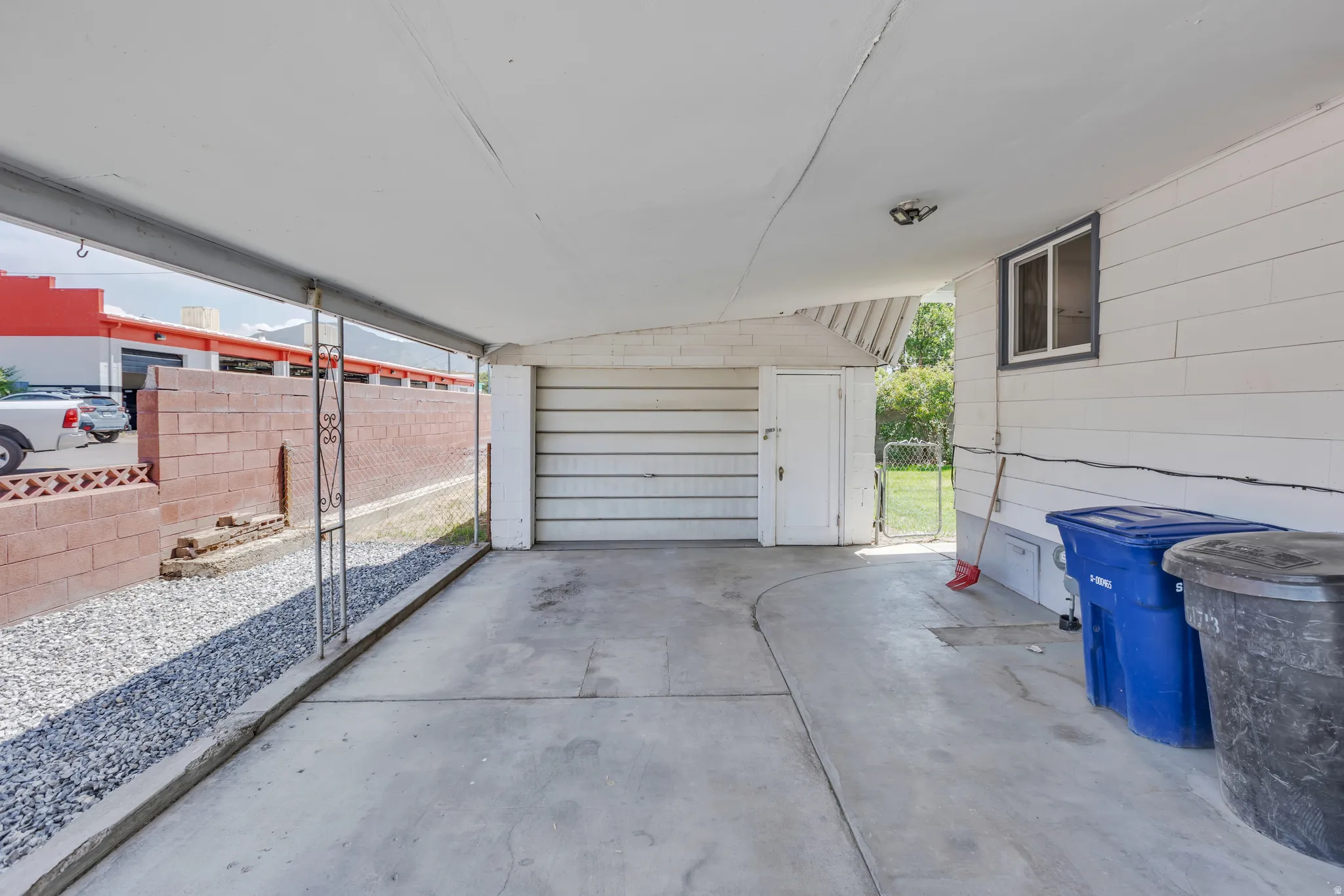 Covered carport with a concrete slab, white horizontal siding, and a white access door